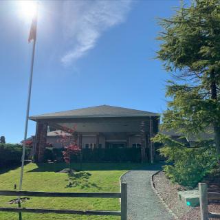 A quaint house with a well-maintained lawn, surrounded by trees and featuring a flagpole, on a sunny day.