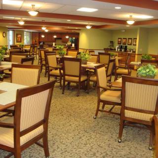 An empty dining area with neatly arranged tables and chairs, warmly lit by ceiling lights.