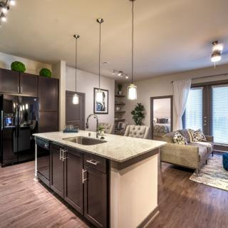 A modern open-concept kitchen and living room featuring hardwood floors, a kitchen island, and pendant lighting.