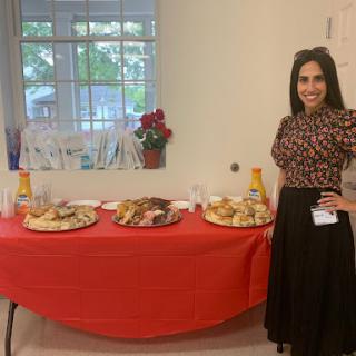 A woman stands beside a table filled with a variety of snacks and refreshments, ready for an event.