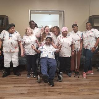 A group of people smiling together indoors, with one person in a wheelchair in front.