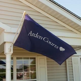 A flag with 'Arden Courts' text displayed outside a building.