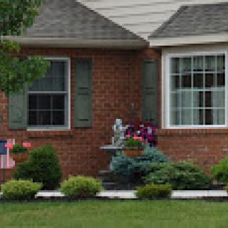 A well-maintained brick house features a charming garden with flowers and a decorative statue.