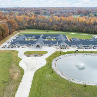 Aerial view of a modern building surrounded by landscaped grounds and a pond, showcasing vibrant autumn colors.