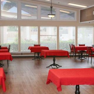 A dining room with tables covered in red tablecloths and large windows allowing natural light.