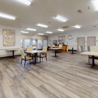 Spacious dining area with tables and chairs, featuring a hardwood floor and bright lighting.