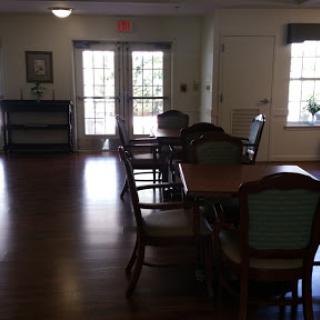 A well-furnished room with tables and chairs, illuminated by natural light from the windows.