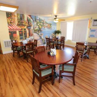 A cozy dining area featuring wooden floors, round tables with chairs, and a scenic mural on the wall.