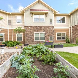 A two-story residential building with a neatly landscaped garden and vegetable plots in the foreground.