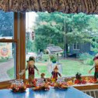 A cozy kitchen with autumn-themed scarecrow decorations overlooks a lush garden through a large window.