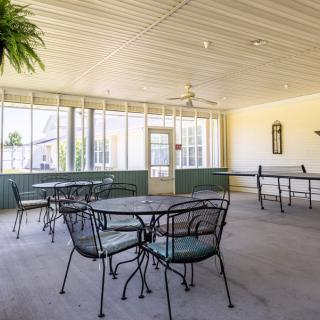 A bright indoor seating area with metal tables and chairs, surrounded by large glass windows allowing natural light to fill the space.