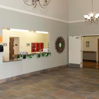 A spacious lobby area featuring a reception window, decorative mirror, and chandelier lighting.