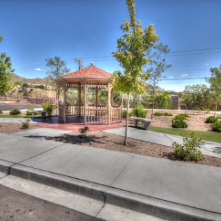 A peaceful park scene featuring a gazebo surrounded by greenery and a clear blue sky.