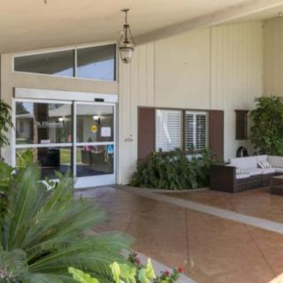 The entrance of a building featuring glass doors, potted plants, and a bench.