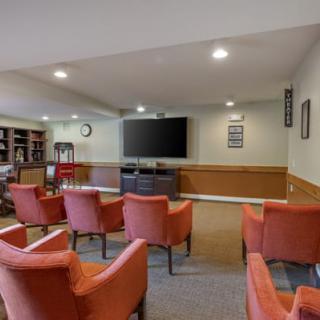 A conference room with multiple chairs facing a large television, featuring a bookshelf and carpeted flooring.