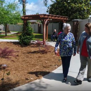 Two people walking along a garden pathway on a sunny day.