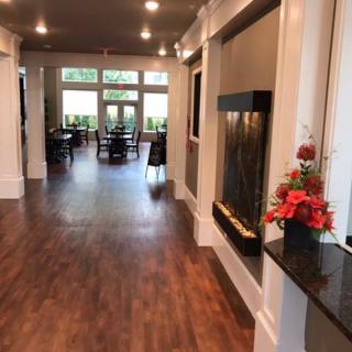 A modern lobby with a hardwood floor and a fireplace, leading into a dining area.
