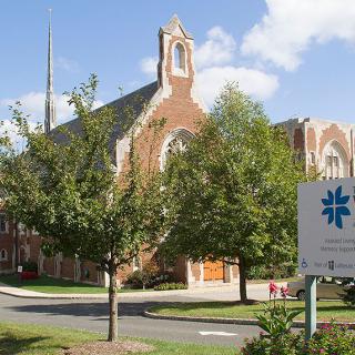 A church with a pointed tower surrounded by trees under a clear blue sky.