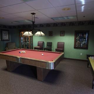 A cozy billiard room with a red pool table, chairs, and warm lighting.