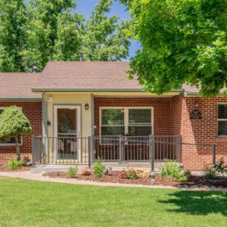 A charming brick house with a small front porch, surrounded by a well-kept lawn and lush green trees.