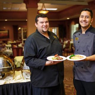 Two chefs proudly display their culinary creations in a restaurant setting.