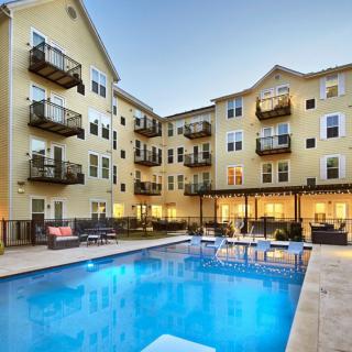 A modern apartment complex featuring an illuminated outdoor pool area during the evening.