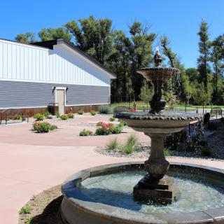 A serene garden featuring a decorative fountain and a landscaped area, set against a clear blue sky.