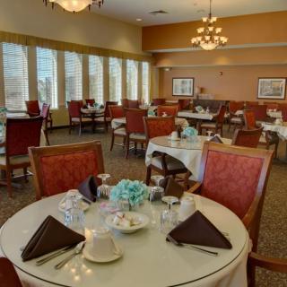 An elegantly set dining room with round tables and red chairs, featuring chandeliers and large windows.