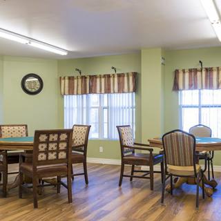 A cozy dining area with tables and chairs, featuring large windows and a wooden floor.