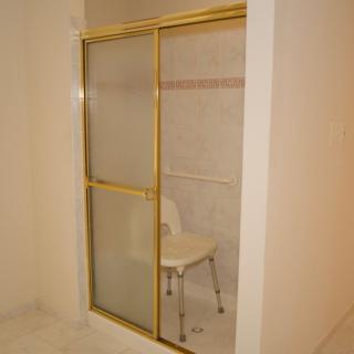 A bathroom shower with a gold-framed sliding door and a chair inside.