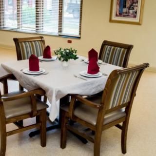 A neatly set dining table with four chairs, adorned with red napkins and a white tablecloth.