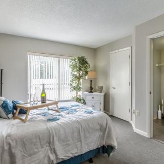 A cozy bedroom with a neatly made bed, featuring a breakfast tray and a bottle, bathed in natural light from the large window.
