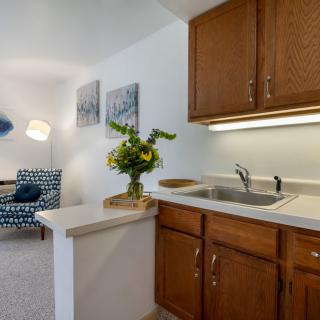 A cozy kitchen area with wooden cabinets, a sink, and decorative elements like flowers and artwork on the wall.