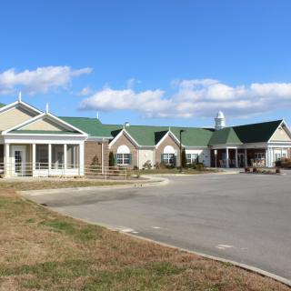 A view of a building with a green roof and parking lot under a clear sky.