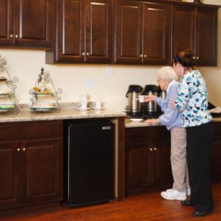 A caregiver assists an elderly individual in a modern kitchen setting.