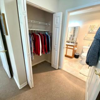 A view of an open closet with clothes and a doorway leading to a bathroom.