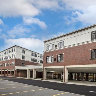 A modern school building with brick exterior and large windows under a partly cloudy sky.