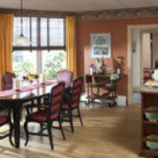 A cozy dining room with a wooden table and chairs, featuring large windows with yellow curtains.