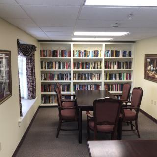 A quiet library room with bookshelves and a central table surrounded by chairs, ideal for reading or study sessions.