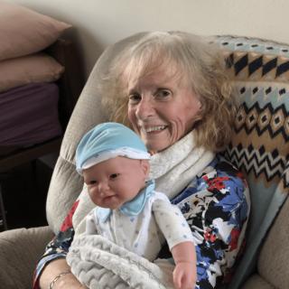 A woman sitting in a chair, holding a smiling baby wrapped in a blanket.