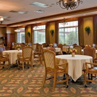 A spacious dining room with elegantly arranged tables and chairs, featuring chandeliers and large windows.