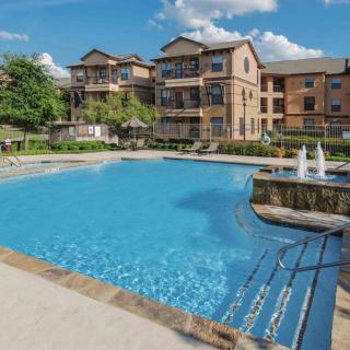 A beautifully maintained swimming pool area in an apartment complex surrounded by residential buildings and greenery.
