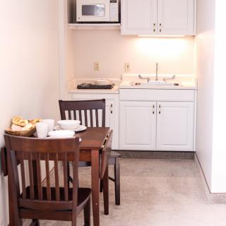 A compact kitchenette with a dining table and chairs, featuring a microwave, sink, and cabinetry.