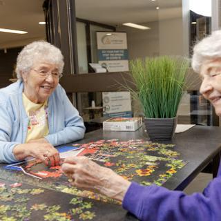 Two elderly women enjoying a puzzle together, fostering friendship and engagement.