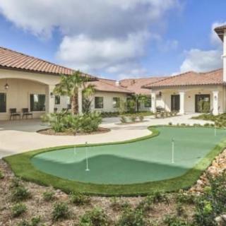 A spacious backyard with a putting green and lush landscaping under a cloudy sky.