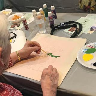 An elderly person engaged in painting at a table, showcasing a creative hobby.