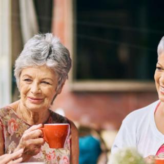 Two senior women enjoying a conversation over coffee outdoors.