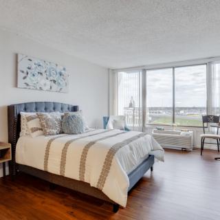 A modern bedroom with large windows, featuring a cozy bed and abundant natural light.