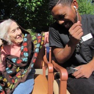 An elderly woman and a caregiver share a joyful moment outdoors.