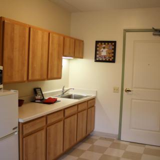 A simple kitchen with wooden cabinets, a refrigerator, and a sink.